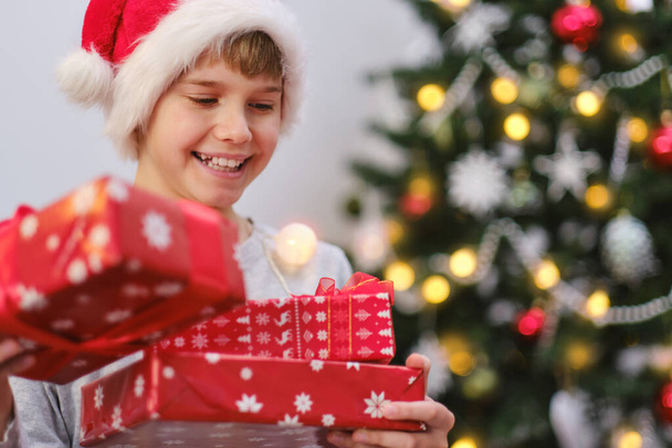 Ένα αγόρι που κρατάει τα δώρα του το πρωί των Χριστουγέννων. Καλά Χριστούγεννα. - Φωτογραφία, εικόνα