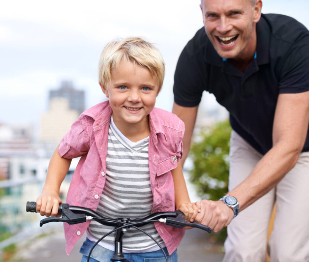 Ξεχωριστές στιγμές πατέρα και γιου. Ένας ευτυχισμένος πατέρας μαθαίνει στο γιο του να κάνει ποδήλατο. - Φωτογραφία, εικόνα