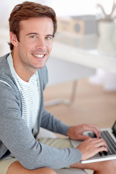 Wiling away the hours online...Portrait of a handsome young man working on a laptop in his living room - Foto, imagen
