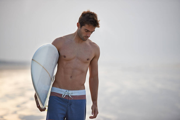 Golven achtervolgen is zijn passie. Een knappe jonge surfer op het strand hunkerend naar een goede golf - Foto, afbeelding
