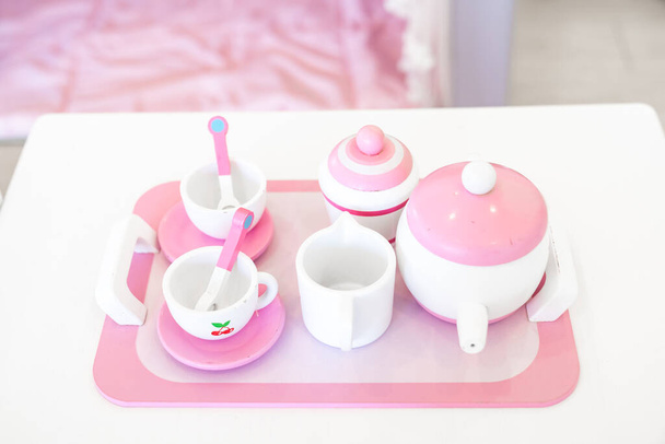 Un set di tazze da tè in legno di colore rosa pastello bianco, tra cui 2 tazze da caffè con cucchiaini, una teiera, un barattolo di zucchero e una brocca di latte viene posizionato su un vassoio.. - Foto, immagini