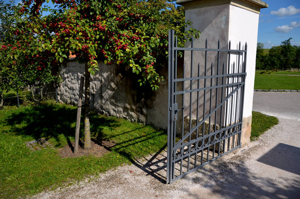 πύλη και φράχτη στο κάστρο στον φθινοπωρινό ήλιο. το πλέγμα που τερματίζει το τέλος των προστατευμένων κλεφτών τοίχων από τους ανάρμοστους εισβολείς. ακίδα σε σχήμα με μεντεσέδες stop και πόρτας, στήλη, τετράγωνο, σοβάς - Φωτογραφία, εικόνα