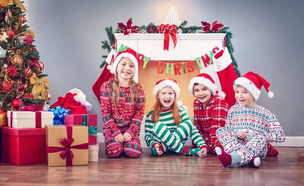 Group of children sitting on the floor indoors on Christmas morning. Concept of the holiday eve and New Year. - Fotoğraf, Görsel