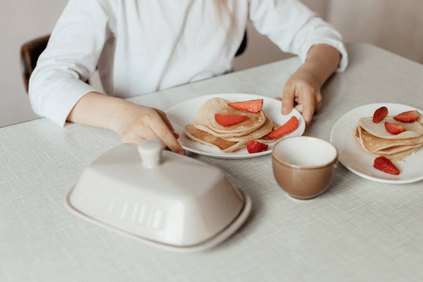 Hungry little girl eat sweet panckaces with strawberries. Family breakfast concept. Children's hands with a plate on which pancakes with strawberries - Zdjęcie, obraz