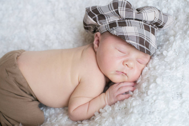 Cute little baby in a plaid vintage cap sleeps on a white boucl bedspread at home. Health and motherhood - Foto, imagen