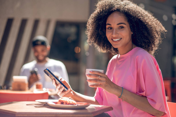 Coffee time. Cute curly-haired young woman in pink shirt in a street cafe - Foto, Imagen