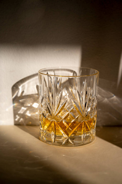Alcohol drink in crystal glasse, sun light, shadows. Brandy or whiskey drink creative natural light - Photo, Image