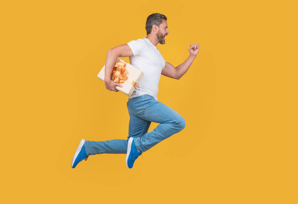 Energetic guy running fast with present box. Present courier in midair yellow background. Gift and present delivery. - Foto, Bild