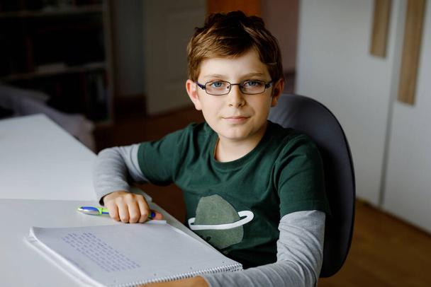 Мальчик в очках учится дома в школе. Ребенок-подросток делает уроки. Концепция домашнего обучения и дистанционного обучения - Фото, изображение