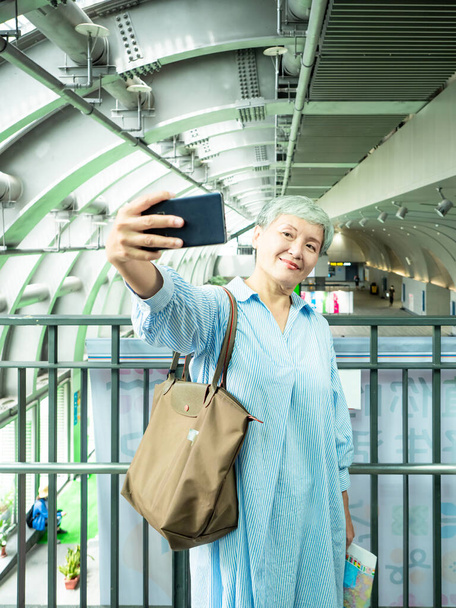 Portrait d'une heureuse femme âgée asiatique âgée des années 60 prenant des photos selfie en utilisant un appareil photo smartphone pour le concept de voyage. - Photo, image
