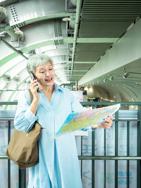 Portret dojrzałej kobiety w wieku 60 lat trzyma mapę i smartfon w koncepcji turystyki do podróży, Podróże lub odkrywania koncepcji. - Zdjęcie, obraz
