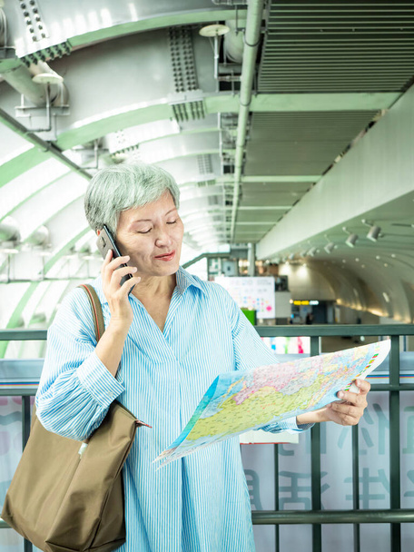 retrato de maduro idade asiática mulher 60s segurando um mapa e smartphone no conceito de turismo para viajar, Viajar ou explorar conceito. - Foto, Imagem