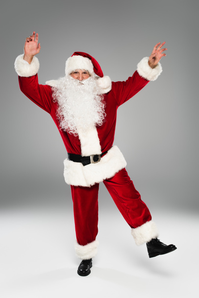 Volle Länge des Weihnachtsmannes im Kostüm, der auf grauem Hintergrund tanzt  - Foto, Bild