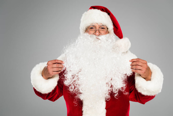 Babbo Natale in occhiali e cappello guardando la fotocamera isolata su grigio  - Foto, immagini