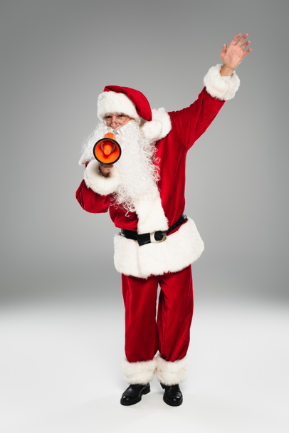 Plná délka Santa Claus v červeném kostýmu drží reproduktor na šedém pozadí  - Fotografie, Obrázek