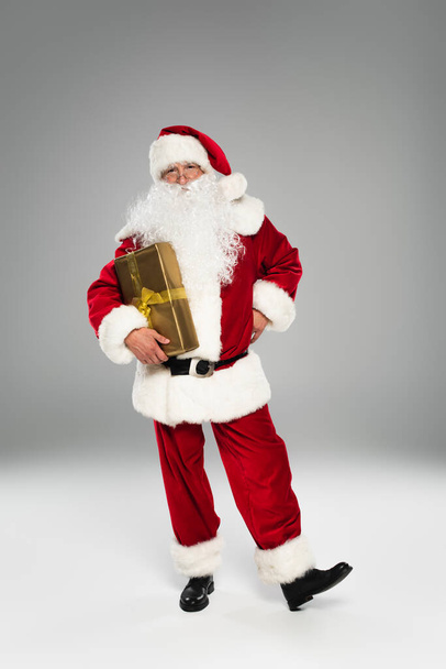 Full length of santa claus with present standing on grey background  - Valokuva, kuva