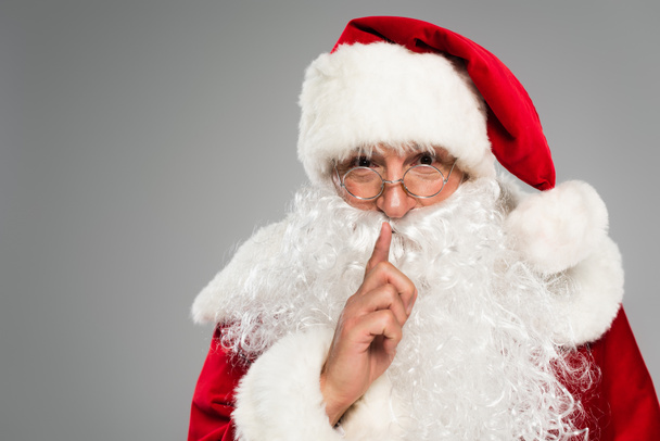 Portrait of father christmas showing secret gesture at camera isolated on grey  - Photo, image