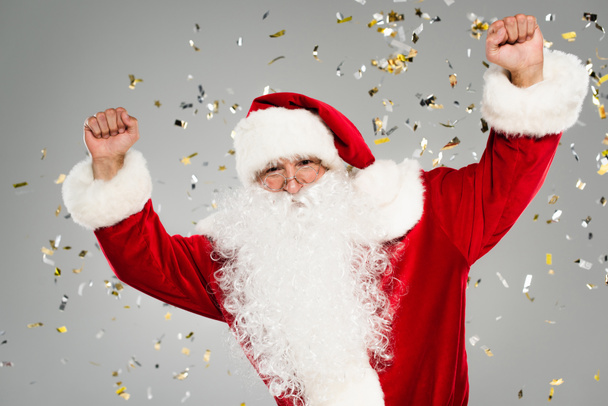 Excited father christmas showing yes gesture under confetti on grey background  - Photo, image