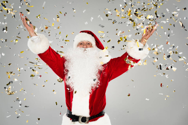 Père Noël dans des lunettes debout sous des confettis sur fond gris  - Photo, image