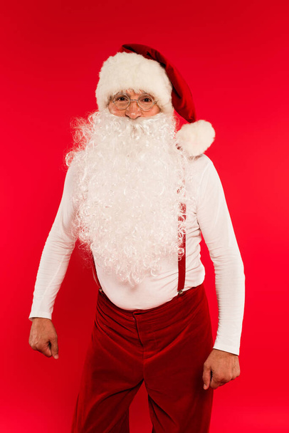 Santa Claus en gafas mirando a la cámara aislada en rojo  - Foto, Imagen