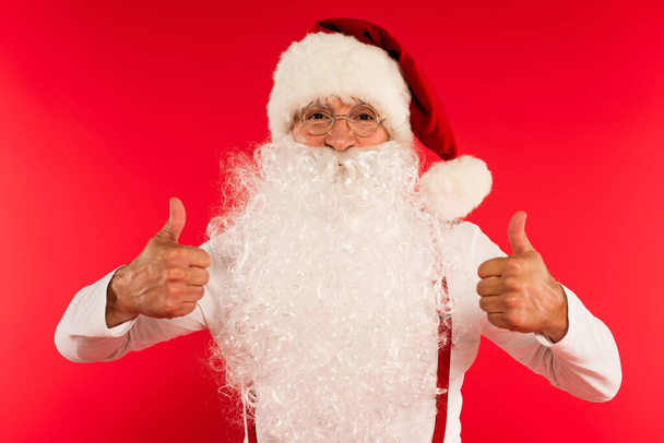 Vousatý otec Vánoce ukazující jako gesto na kameru izolované na červené  - Fotografie, Obrázek