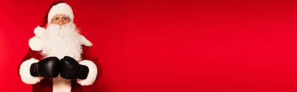 Otec Vánoce v kostýmu a boxerské rukavice na červeném pozadí s kopírovacím prostorem, banner  - Fotografie, Obrázek