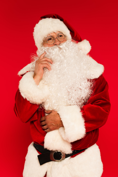 Pensivo Papai Noel em traje olhando para longe isolado no vermelho  - Foto, Imagem