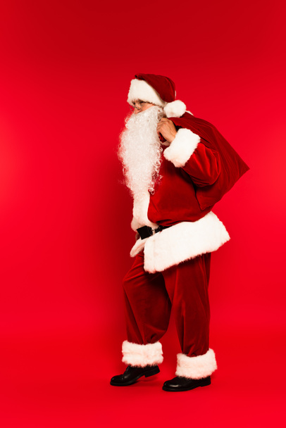 Full length of father chistmas holding sack on red background  - 写真・画像