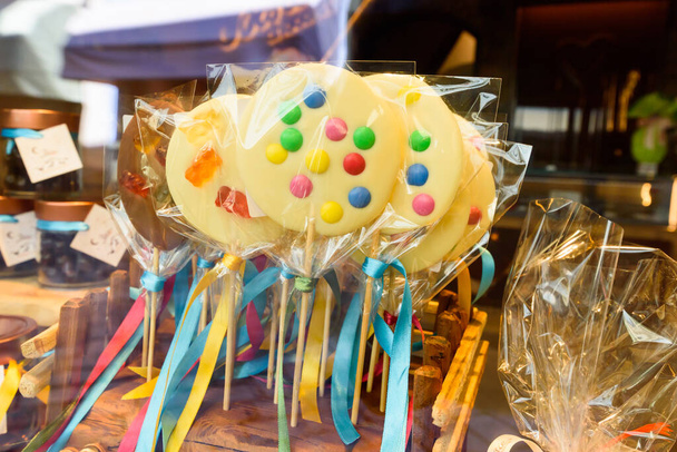 Aoste, Italie. Dans la rue, biscuits emballés recouverts de glaçage jaune avec des points de chocolat colorés, placés sur un cure-dent, avec des rubans pendants, à vendre à l'extérieur d'une boutique. 17 avril 2022. - Photo, image