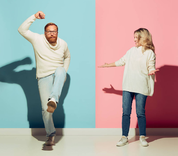 Couple of young happy man and woman dancing, having fun isolated over blue-pink studio background. Human emotions, youth, love, relationship and active lifestyle concept. Models in casual clothes - Fotó, kép