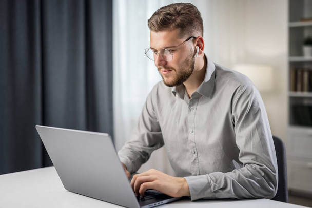 Handsome man in grey shirt coding at laptop from home, remotely work writing code - Fotó, kép