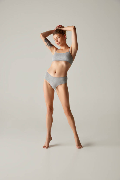 Full-length portrait of slim young woman posing in underwear isolated over grey studio background. Feeling good . Concept of beauty, body and skin care, health, plastic surgery, cosmetics - Fotó, kép