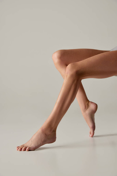 Cropped smooth female legs isolated over grey background. Taking care after skin. Depilation, epilation. Concept of beauty, body and skin care, health, plastic surgery, cosmetics. Copy space for ad - Fotoğraf, Görsel