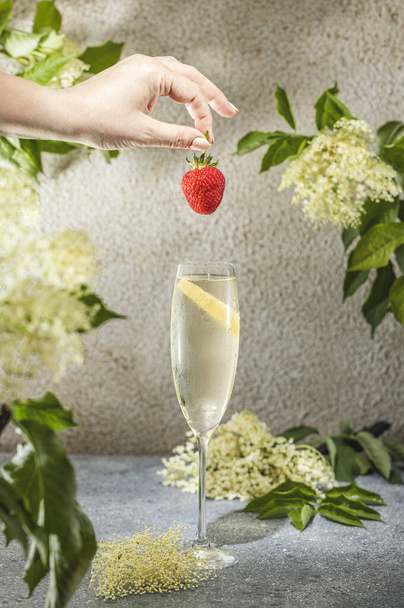 Vera donna che prepara l'Elder Fashion Royal Cocktail in vetro Champagne circondato da ingredienti e strumenti da bar sulla superficie grigia del tavolo. Bevanda rinfrescante pronta per bere. - Foto, immagini