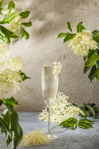Elder Fashion Royal Cocktail im Champagnerglas umgeben von Zutaten und Barwerkzeugen auf grauer Tischoberfläche. Erfrischendes Getränk zum Trinken bereit. - Foto, Bild