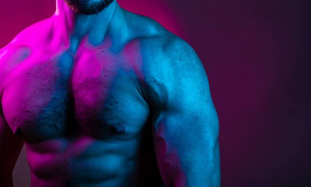 Sportive man bodybuilder is posing in the colorful neon light with naked muscular torso showing chest, abdominal muscles in neon studio light. - Photo, image