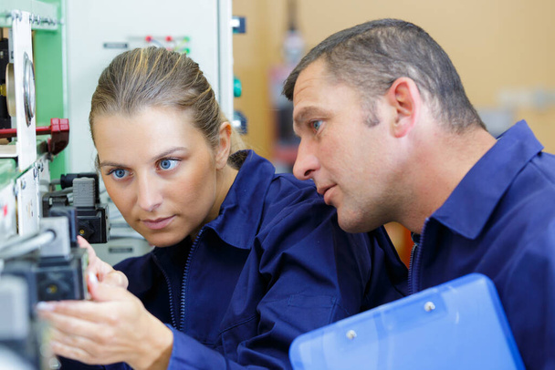 supervisor watching over female apprentice setting up machine - Fotoğraf, Görsel