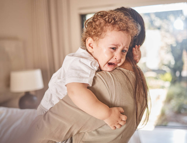 Crying, sad and tears of baby with mom for comfort, safety and attention while hungry, upset or tired in a family home. Toddler boy child cry while in arms of caring woman babysitter, mother or nanny. - 写真・画像