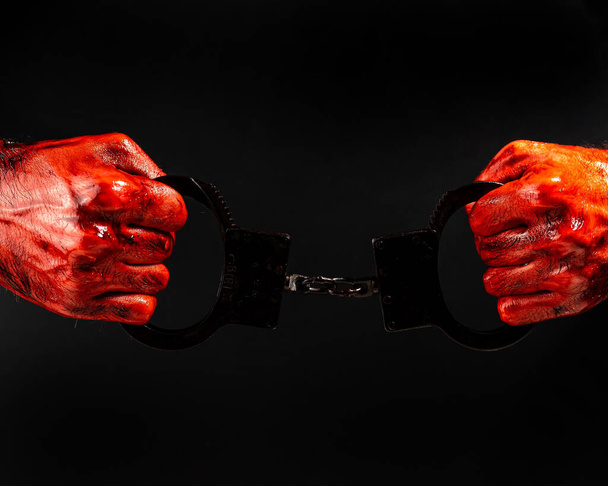 A man with bloody hands holds iron handcuffs - Фото, зображення