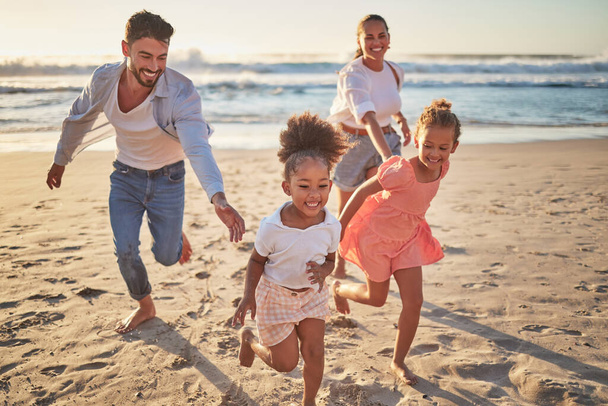 Family, beach and kids with parents running on sand on summer holiday. Mom, dad and children at ocean at sunset in Mexico. Freedom, fun and vacation, happy man and woman playing with girls at the sea. - Photo, image