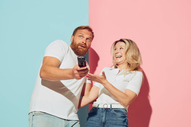 Emotional young couple, bearded man and pretty woman isolated over blue-pink studio background. Human emotions, youth, love, relationship and active lifestyle concept. Models in casual clothes - Φωτογραφία, εικόνα