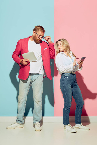 Studio shot of couple of young funny and happy man and woman having fun isolated over blue and pink background. Human emotions, youth, love and active lifestyle concept - Foto, Imagen