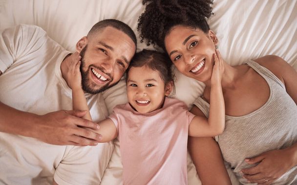 Family happy, child and above bed with parents in the morning, funny face in house and relax after sleeping together in home. Portrait of happy mother and dad smile with girl kids in home bedroom. - Fotó, kép