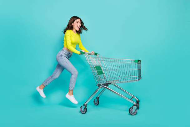 Full size profile photo of cool brunette hair young lady run with trolley wear shirt jeans sneakers isolated on teal color background. - Φωτογραφία, εικόνα