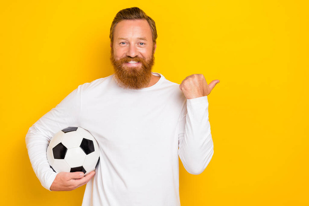 Photo of cheerful person arm hold football direct thumb finger empty space isolated on yellow color background. - 写真・画像