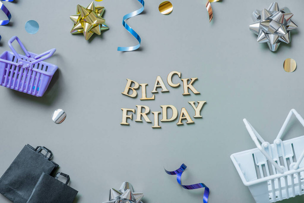 Black friday text with gifts, shopping baskets and bags and festive tinsel flat lay. - Photo, Image