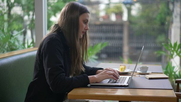 Откровенная молодая женщина использует ноутбук в кофейне. Человек, работающий за компьютером в кафе-ресторане и выполняющий удаленную работу. Девочка печатает на клавиатуре письмо - Фото, изображение