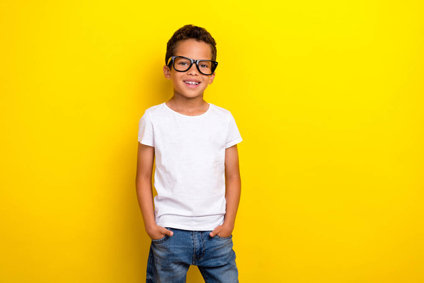 Photo of cool small boy wear white t-shirt eyewear jeans isolated on yellow color background. - Foto, Imagen