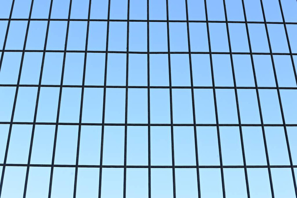 Detalle de una reja o malla de hierro con el azul del cielo de fondo - Foto, Imagem