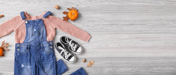 Модний дитячий одяг, взуття та осінній декор на сірому дерев'яному фоні з простором для тексту
  - Фото, зображення